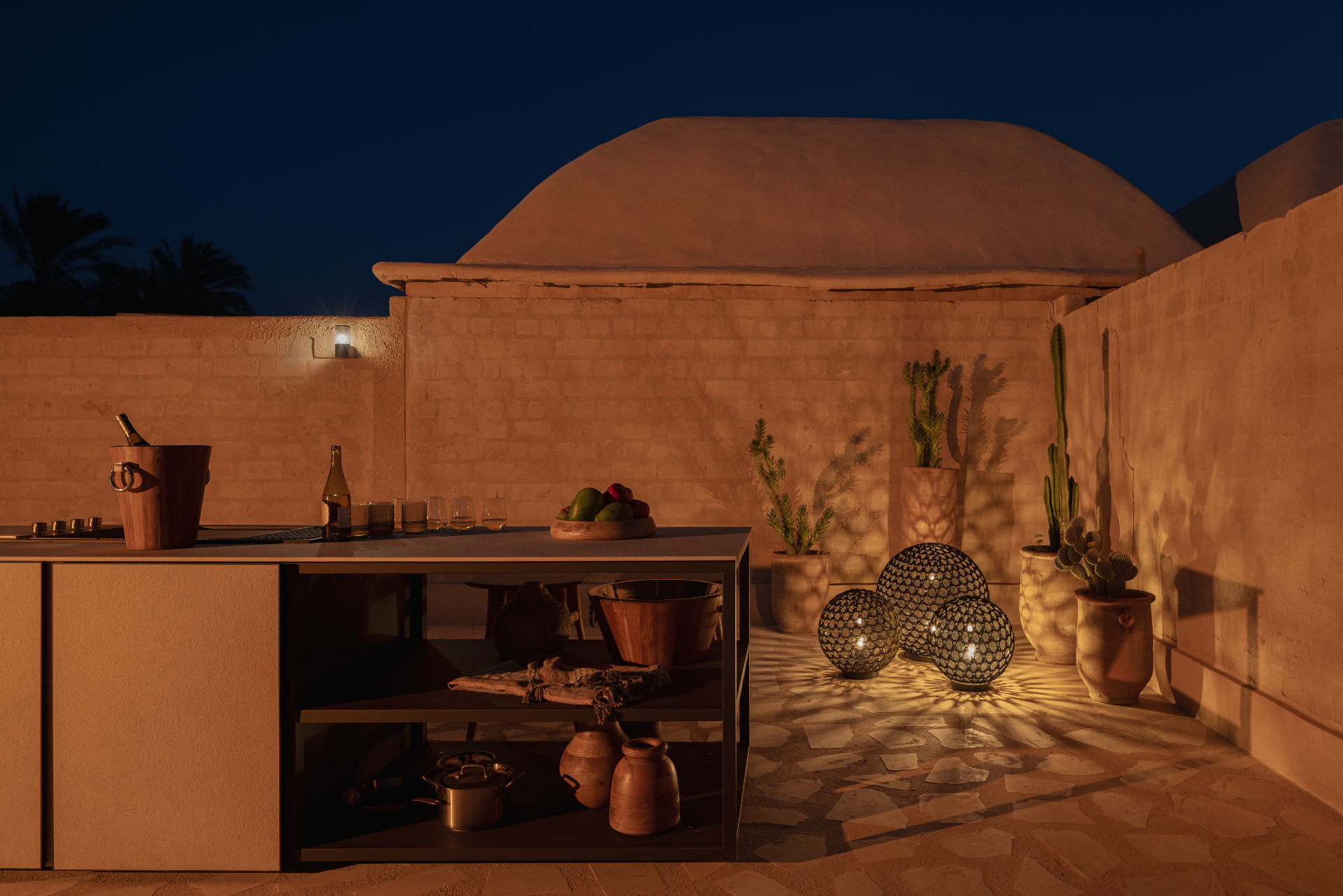 STRATO outdoor kitchen at night with copper pots and lanterns