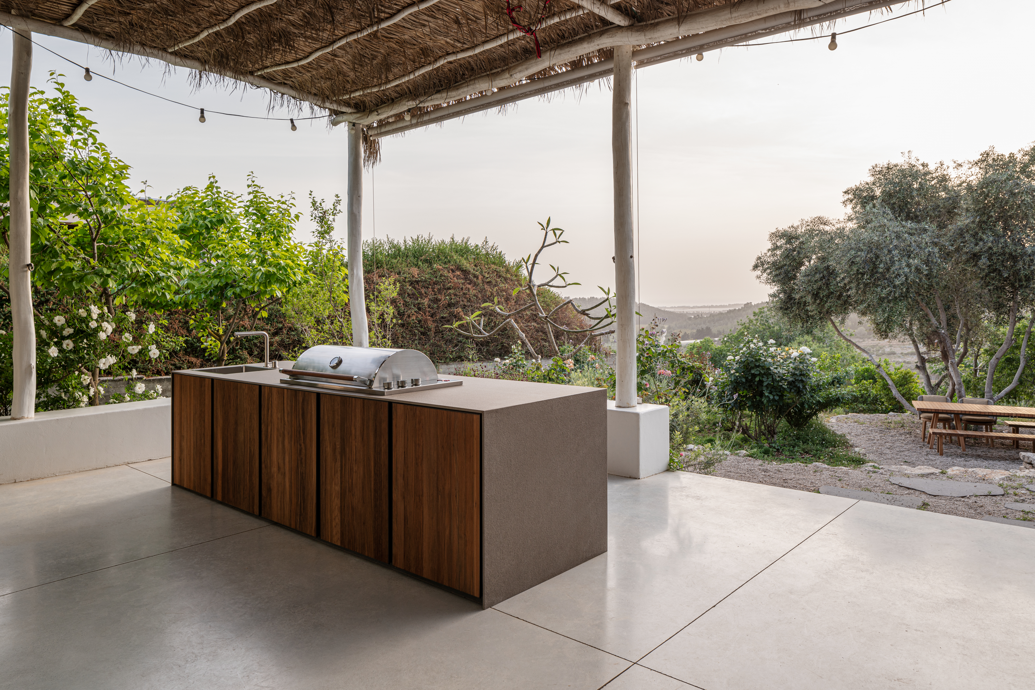 STRATO timber-slat island under a thatch pergola with valley view